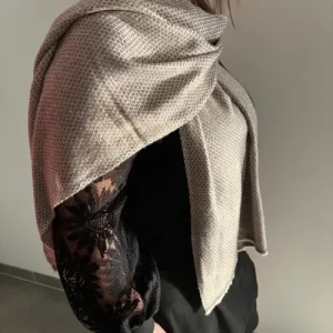 Écharpe en laine du Cachemire couleur beige portée avec élégance avec tissage fin en losange, douce et légère, fabriquée artisanalement. Élégante et intemporelle, parfaite pour toutes les saisons.