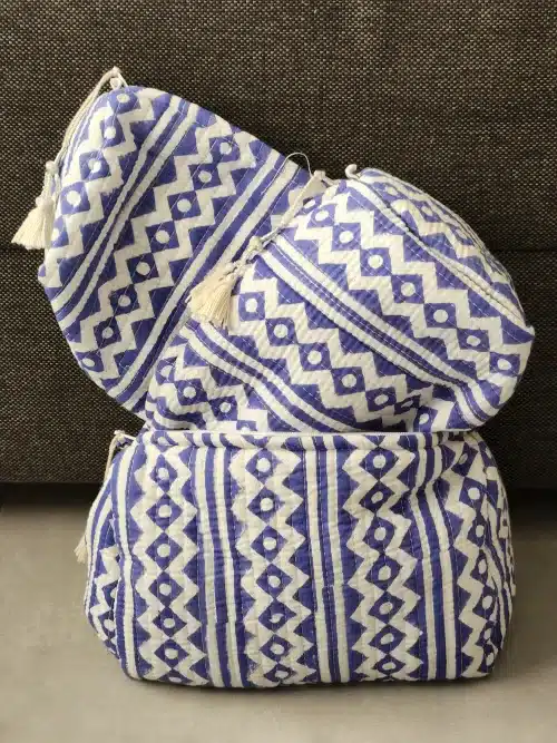 Ensemble de trois trousse de toilette inde bohèmes NEELA fermées, présentant un motif géométrique bleu et blanc et des pompons blancs décoratifs.