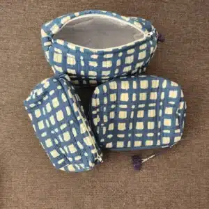 Comparaison des trois tailles de la trousse de toilette indienne KARTI : petite, moyenne et grande, avec motif artisanal à carreaux abstraits bleus et pompons violets.
