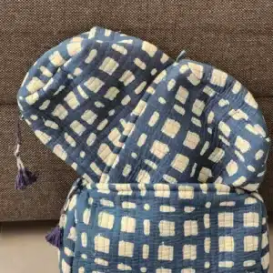 Différentes tailles de trousses de toilette artisanales KARTI en coton matelassé avec motif abstrait bleu et détails de pompons violets.