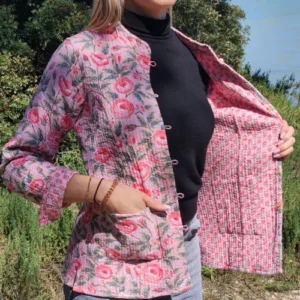 Femme portant la veste kantha réversible rose Priya, manches longues, motif fleuri rose sur fond pastel.